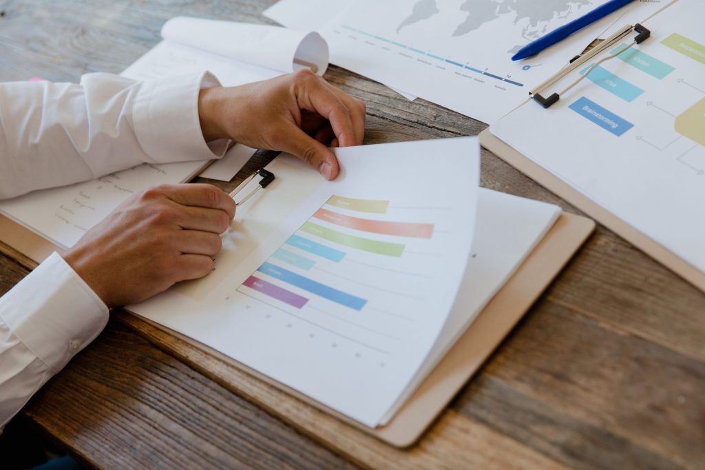 PIB menor e juros ainda altos colocam economia brasileira sob pressão em 2026 Mãos analisam um relatório financeiro com gráficos coloridos sobre uma mesa.
